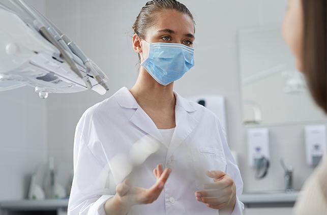 Dentist wearing protective face mask talking to patient