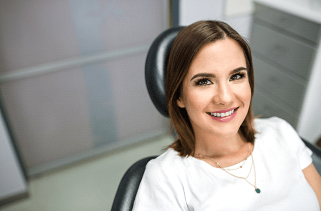 Woman in white shirt smiling in dentist's treatment chair