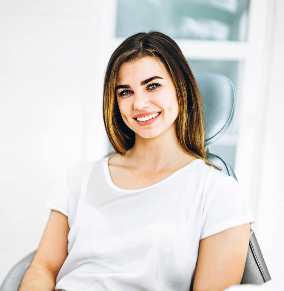 Mujer con camisa blanca sonriendo mientras está sentado en el sillón dental