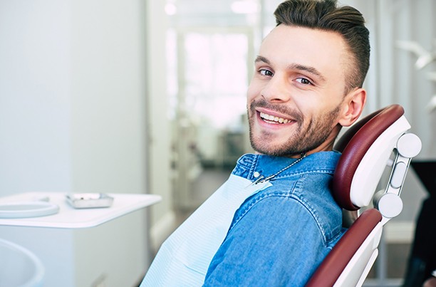 Hombre sonriendo en el sillón dental mientras usa camisa vaquera