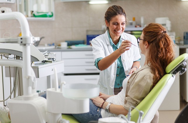 Smiling dentist talking to patient and examining their teeth