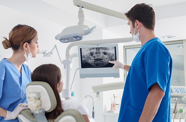Dentist team member and dental patient looking at digital x-rays