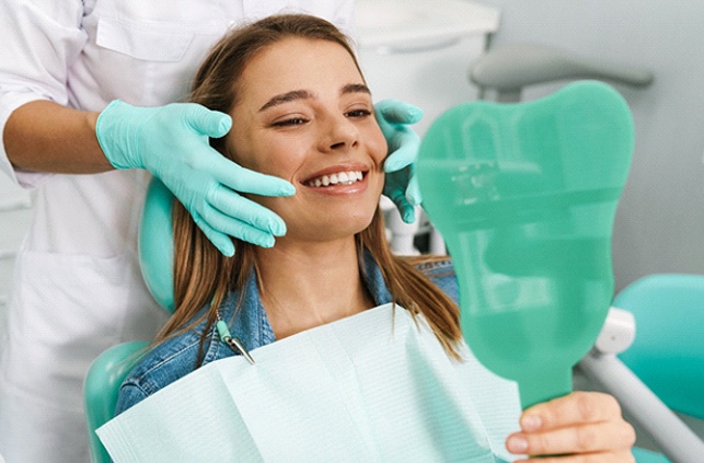 Patient with veneers in Fitchburg smiling in dentist's mirror