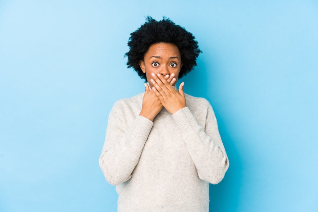 Closeup of patient covering her teeth against blue background